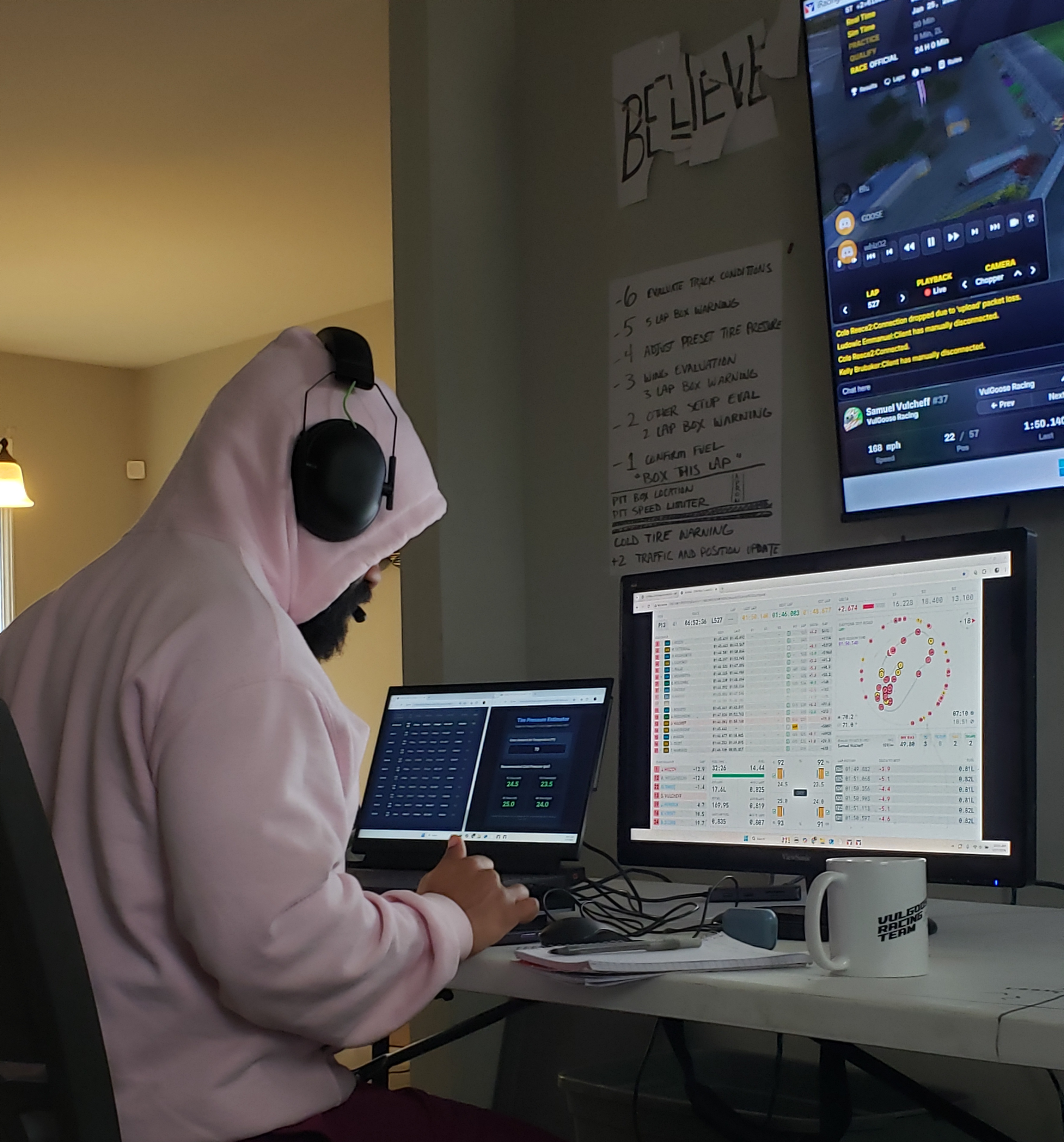 Team member running race engineering during the Rolex 24 at Daytona, timing screens and pit notes in the background