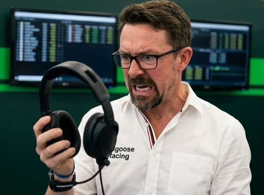 Sam glaring at his headset, holding it out in front of him like it owes him money